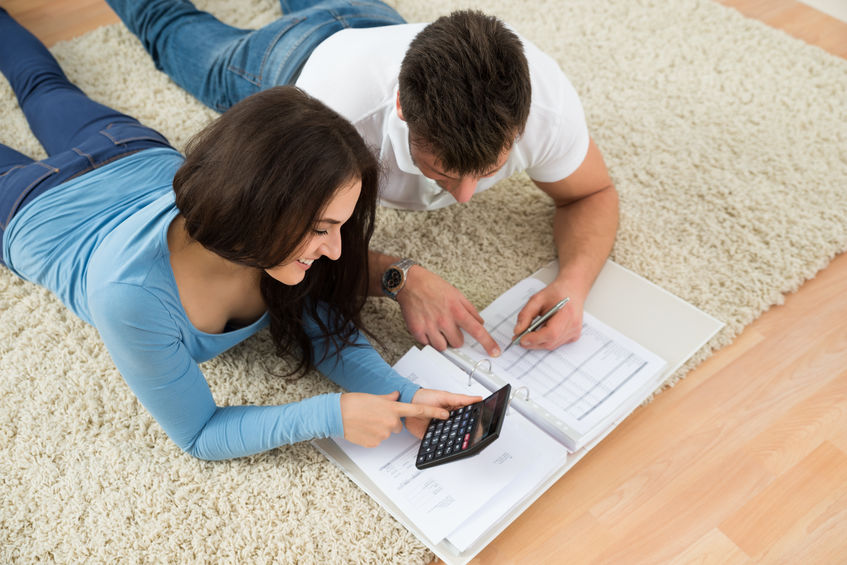 Portrait Of A Happy Young Couple Lying On Rug Calculating Invoice