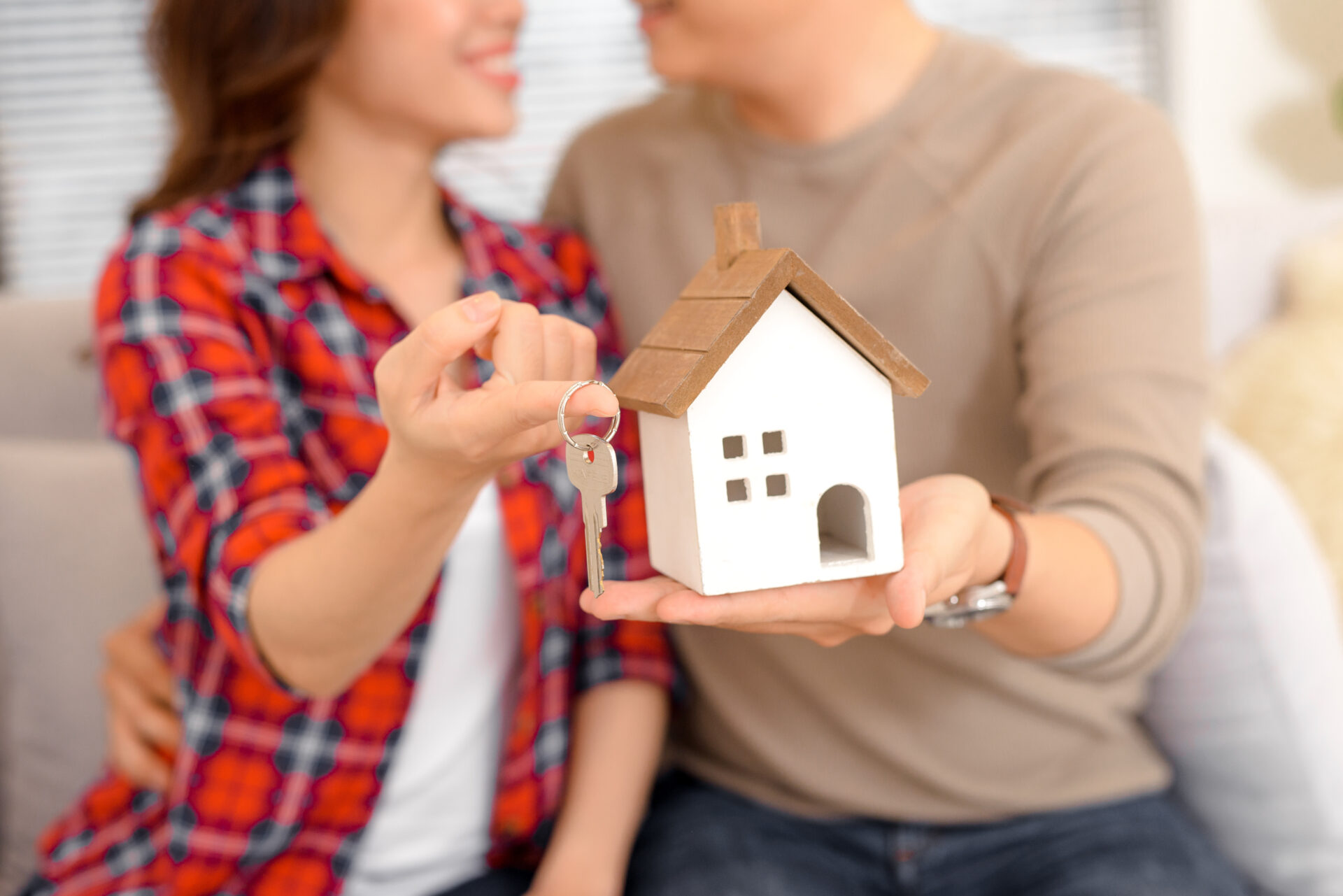 Happy couple holding keys to new home and house miniature