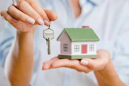close up of woman holding house keys in one hand and a home model in the other